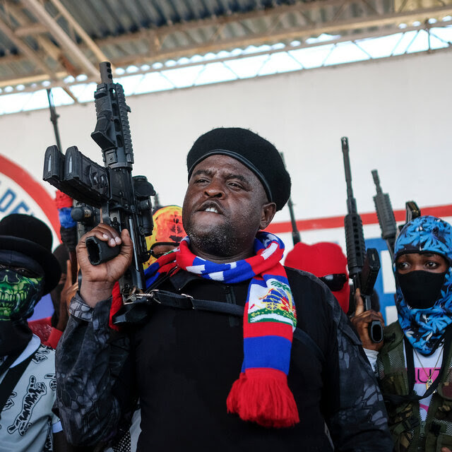 Men stand in formation and hold rifles pointed toward the ceiling. Some wear masks. 