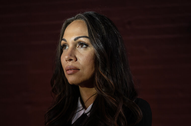 A woman with long hair and business clothes folds her arms as she poses for a photo.