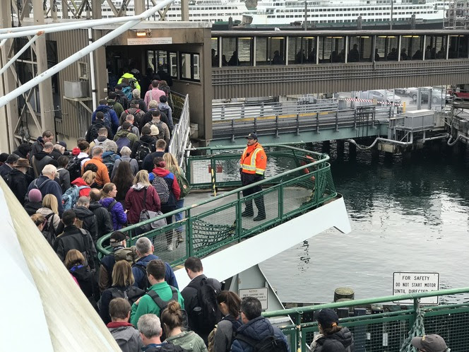 Several people disembarking a ferry from the passenger cabin level while a crewmember watches on