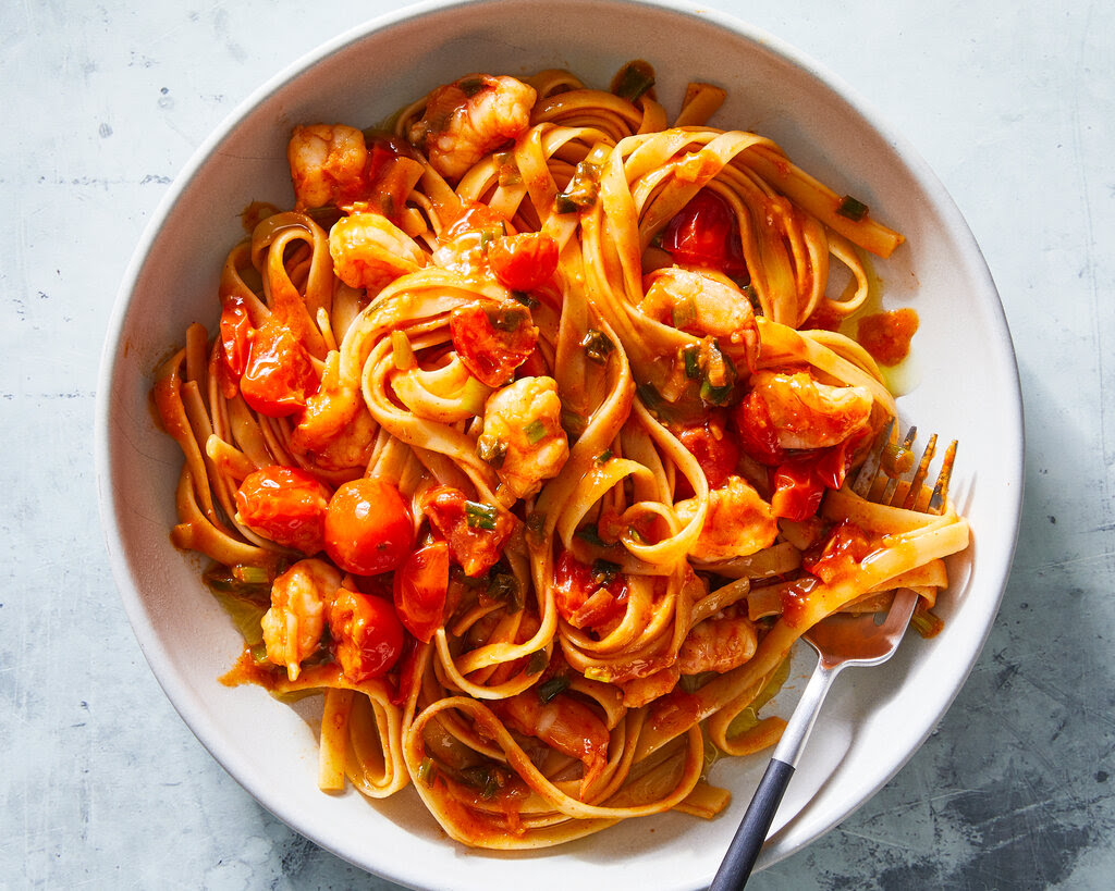 A bowl of thick noodles with tomatoes and shrimp in a red gochujang sauce.