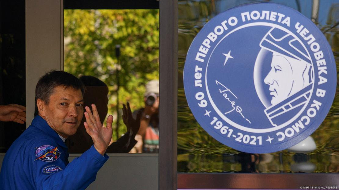 Kononenko acena em frente a logo da Roscosmos