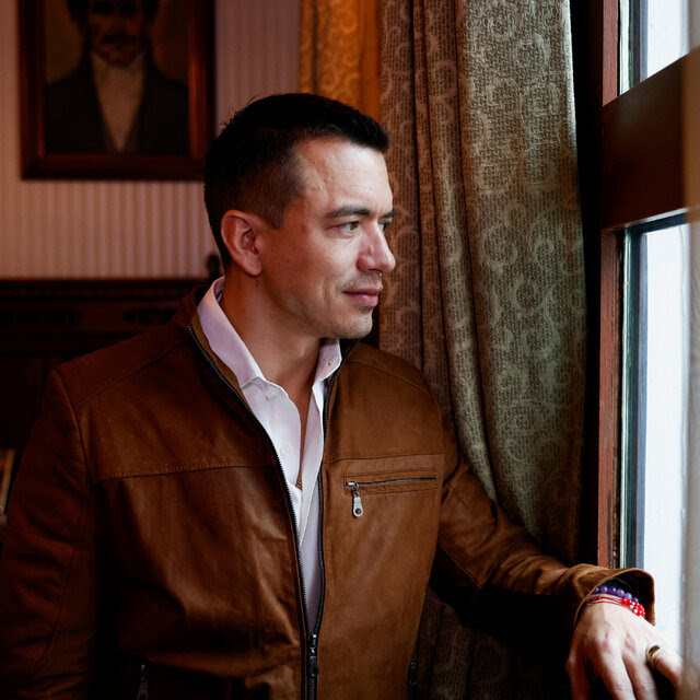 President Daniel Noboa of Ecuador, in a white shirt and brown jacket, gazes out a window. 