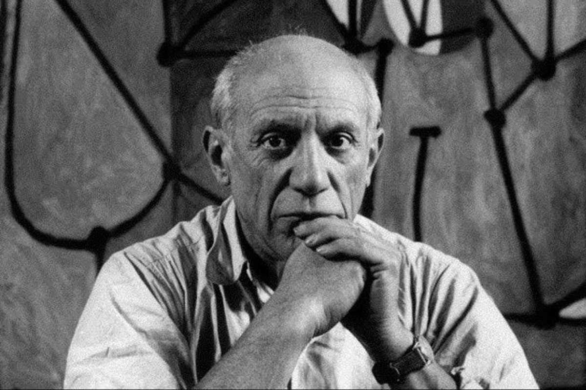 Pablo Picasso sits staring solemnly at the camera, his chin resting on his hands