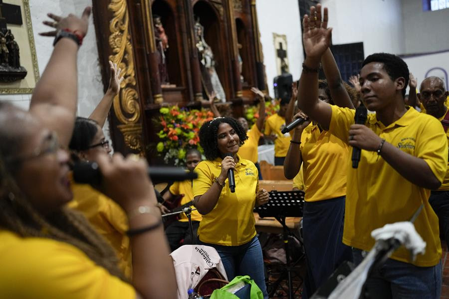 Panamanian people in yellow shirts sing and dance together in a church.