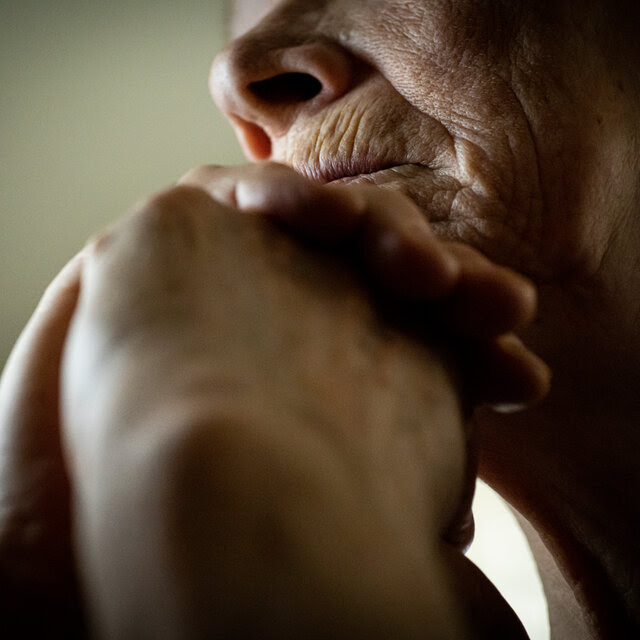 A close-up of a mature adult woman leaning her head onto her hands.