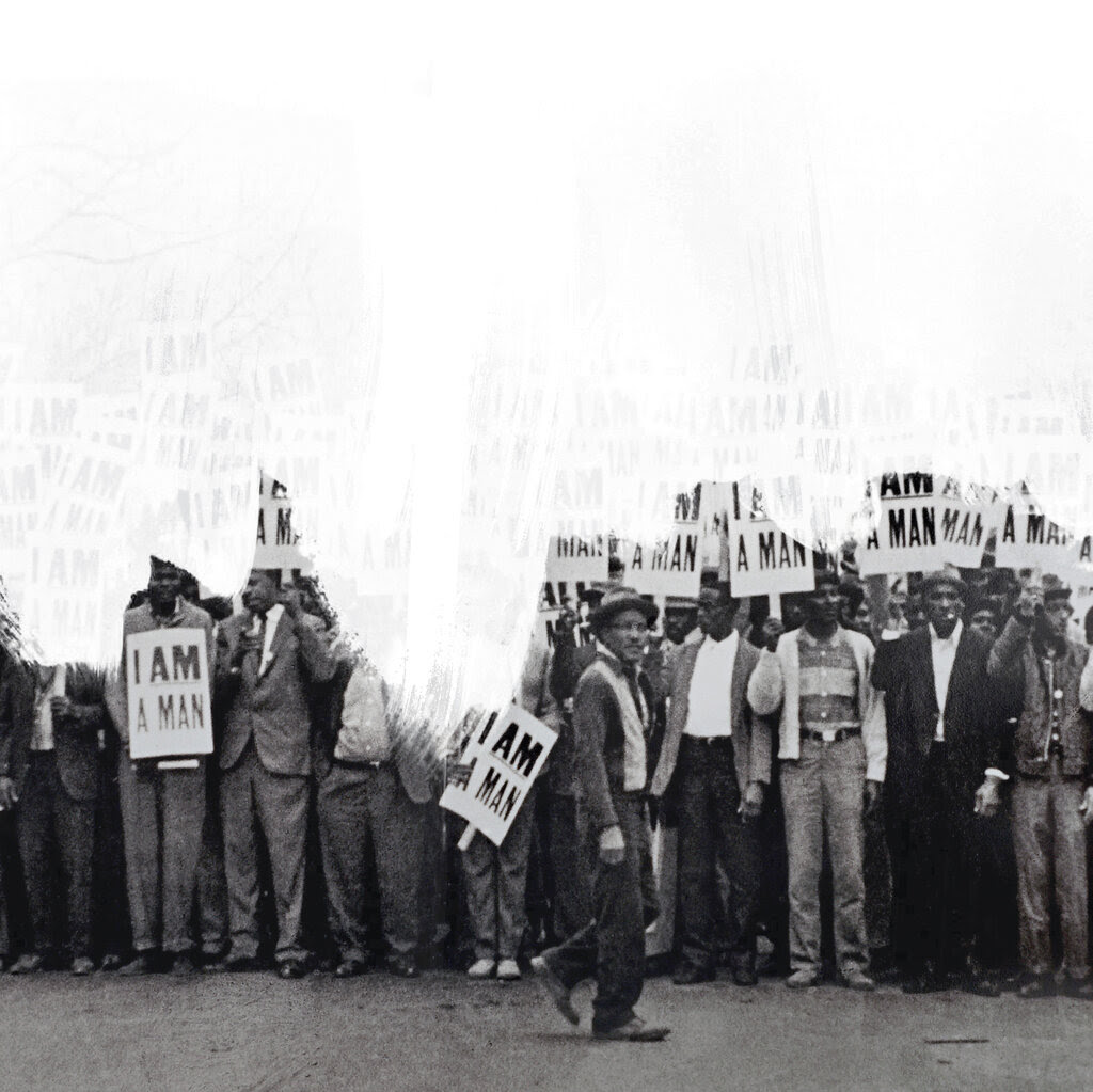 A line of Black protesters hold signs saying “I Am a Man” with white paint added on top of the photograph.