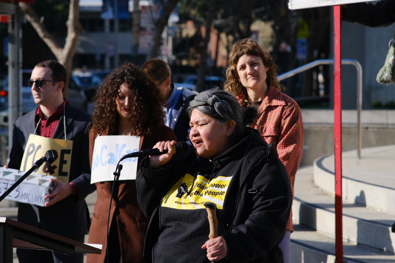 Picture of speaker at rally against rate hike and decision to
keep Aliso Canyon Gas Facility open indefinitely with a shirt that
says Clean Power for the People. Behind the speaker are rally
attendees wearing signs that say PG&E and SoCal Gas. The attendee
wearing the PG&E sign has a box that says $723 Million on it.