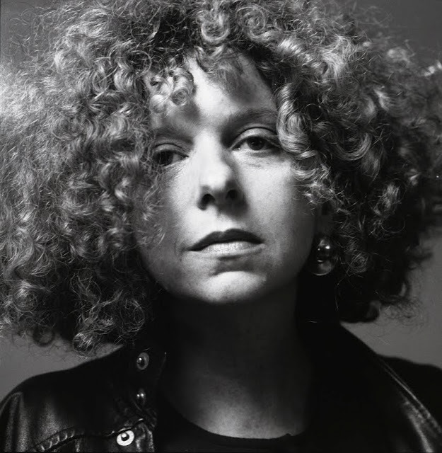 In this black-and-white photo, curly-haired Barbara Kruger, wearing a leather jacket, stares at the camera with intensity.