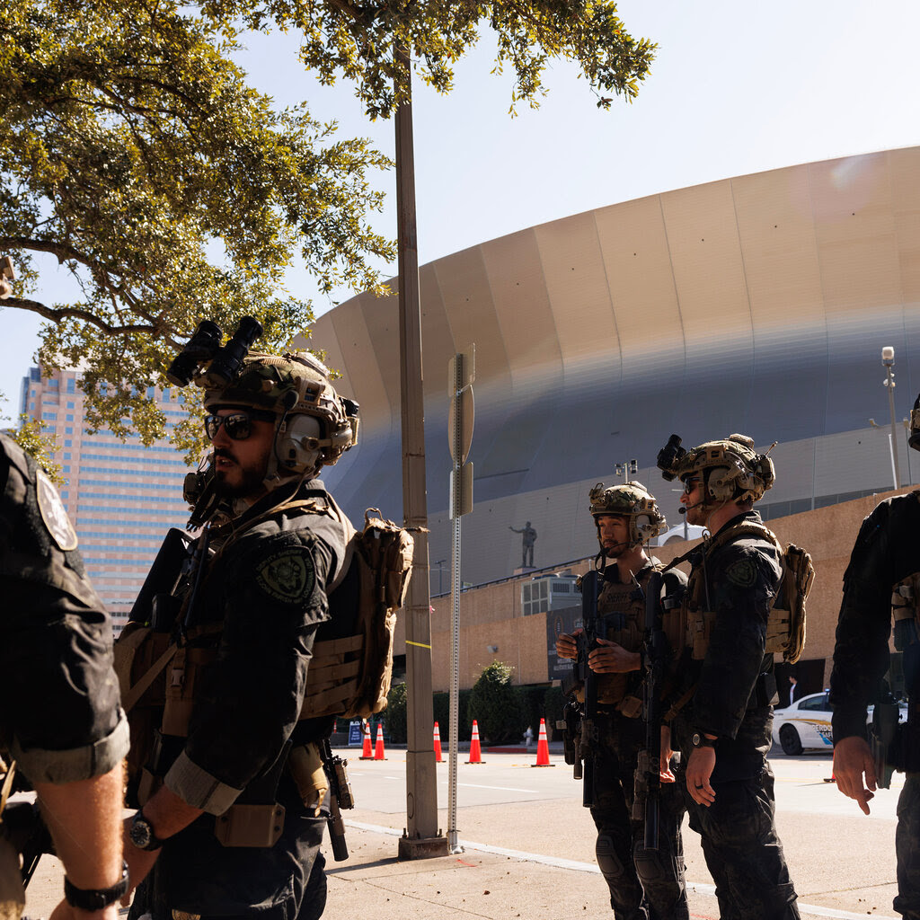 SWAT team members, all holding rifles, stand in front of a large stadium.