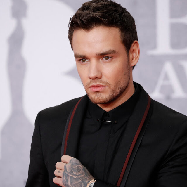 Liam Payne wearing a black shirt and black coat with red trim.