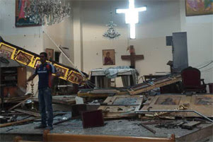 A man is standing amidst debris and broken-down icons in the aftermath of the bombing.