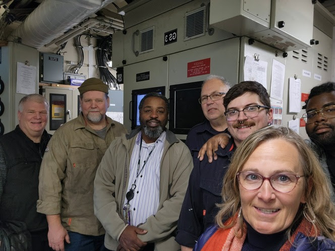 Seven people posing for a selfie in the engine room of a ferry