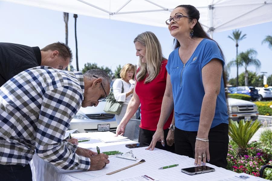 Volunteers stand at a table during a voter registration event. There are also people filling out forms laid out on the table.