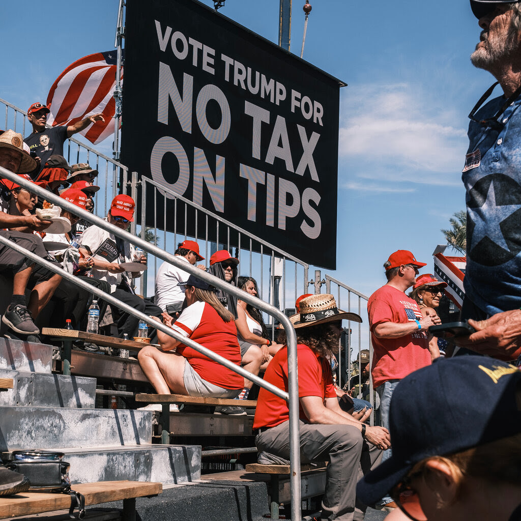 Benches at a rally with a sign that says “Vote Trump for no tax on tips.” 