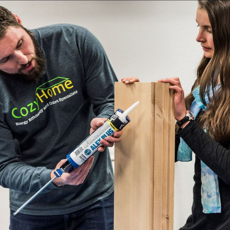 a man and a woman applying caulk on a piece of wood