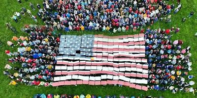 Crowd holds up colored papers to collectively reveal a giant American flag