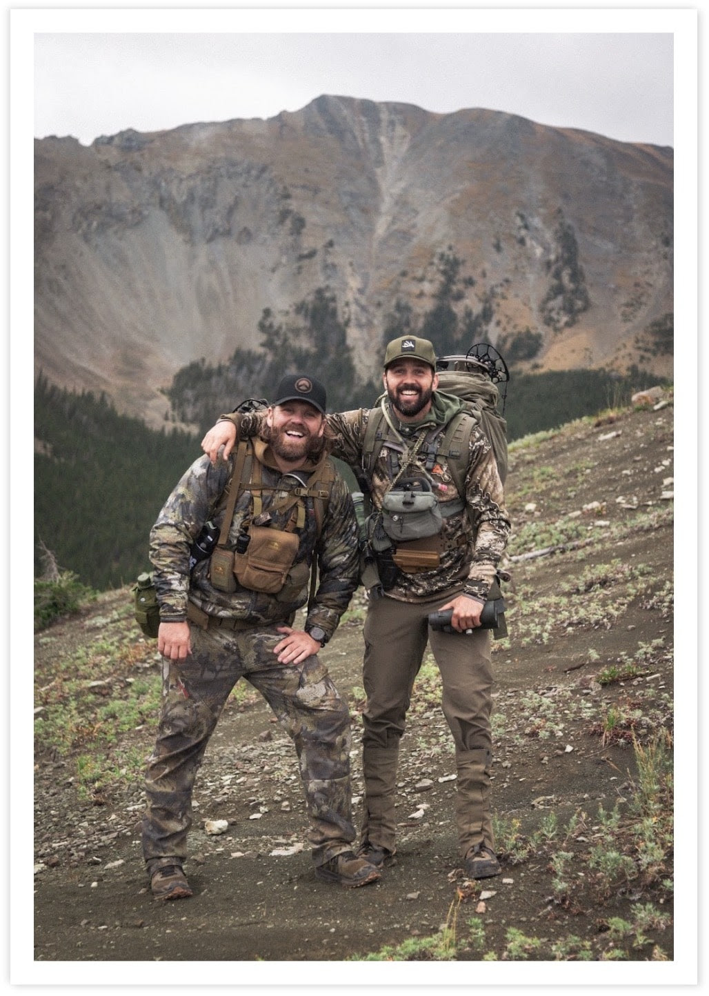 two men in camouflage gear standing on a mountain
