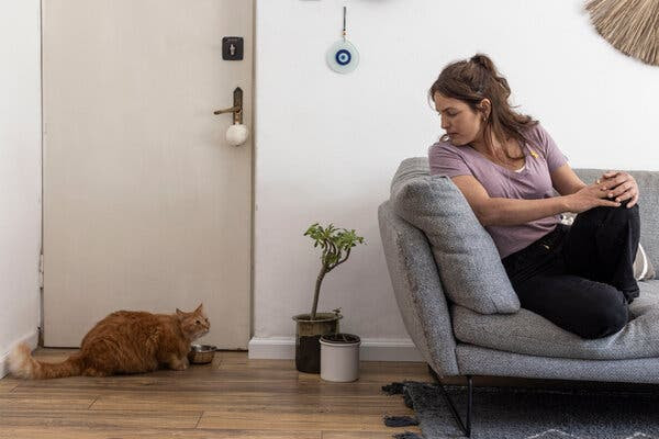 A woman sitting on a couch with her legs up. Nearby is a cat.