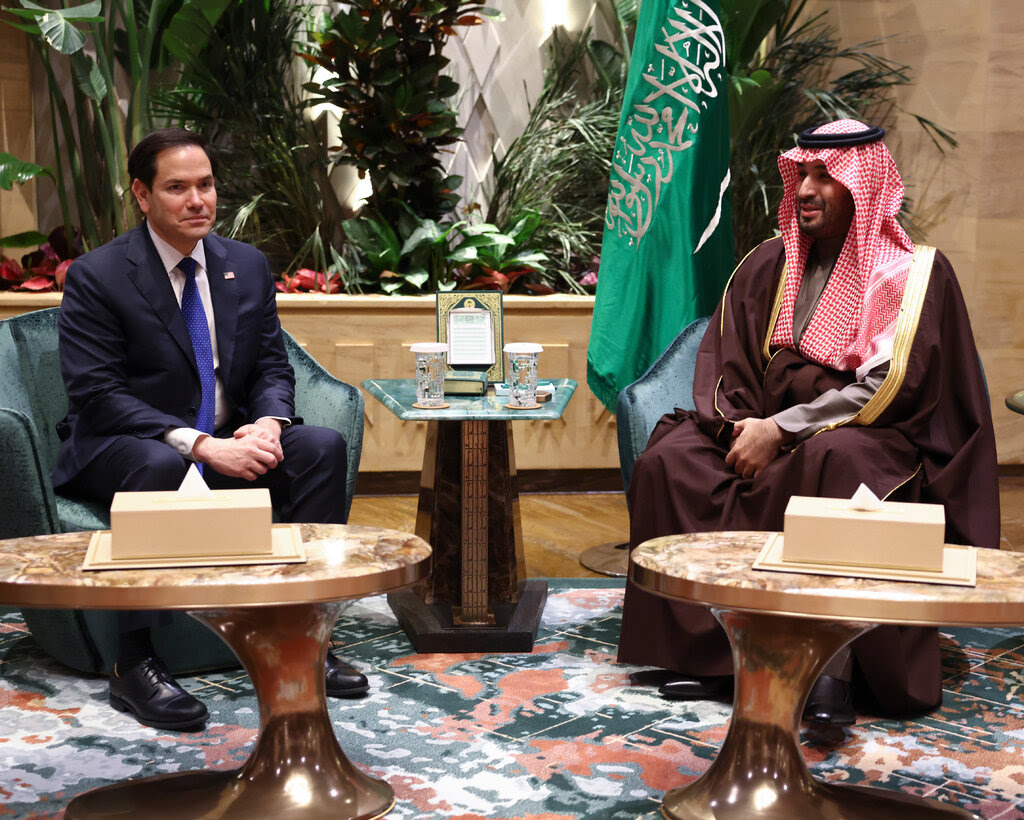 Mr. Rubio in a blue suit and Prince bin Salman in a brown robe and red-and-white headdress, seated across a small table. 