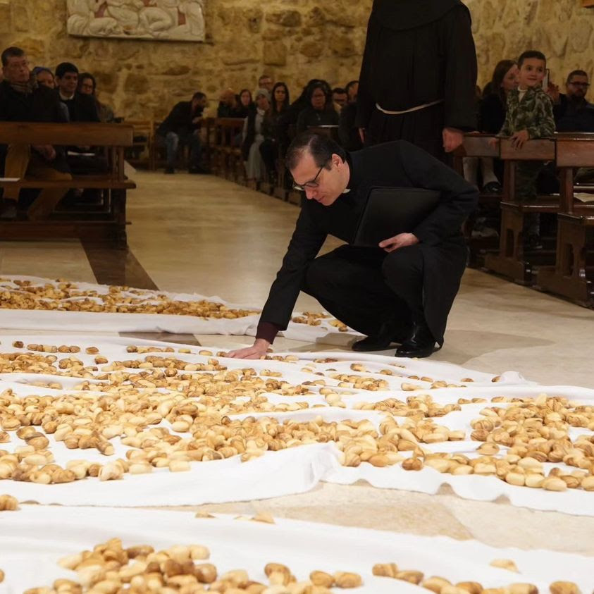 A clergyman praying over thousands of olive wood hearts on white cloth in December 2023, on the Feast of the Holy Innocents, at St. Francis Chapel in the Nativity Church in Bethlehem.