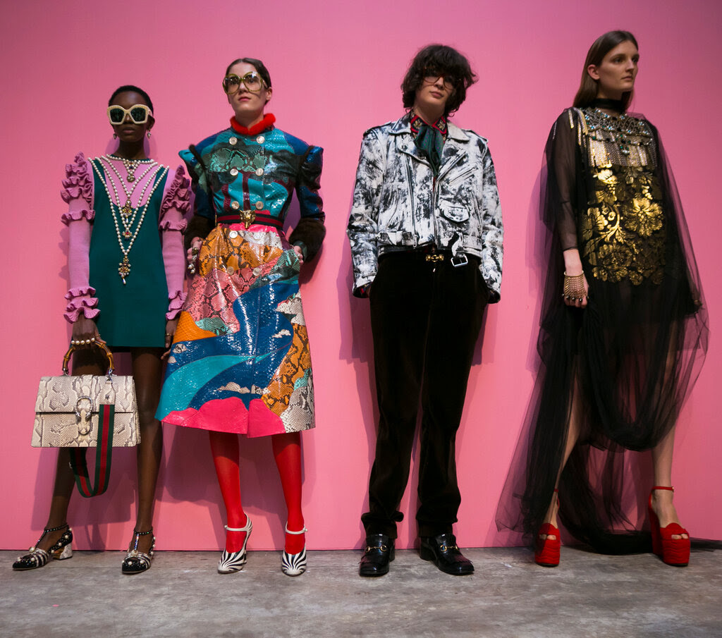 Three women and a man pose against a hot pink backdrop in a magpie combination of print looks designed by Mr. Michele. 