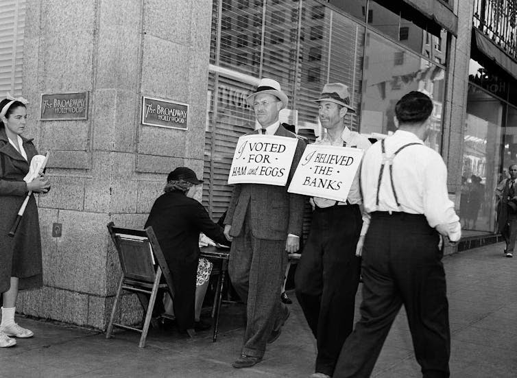 Men walk down the street wearing billboards, one saying 'I believed the banks'