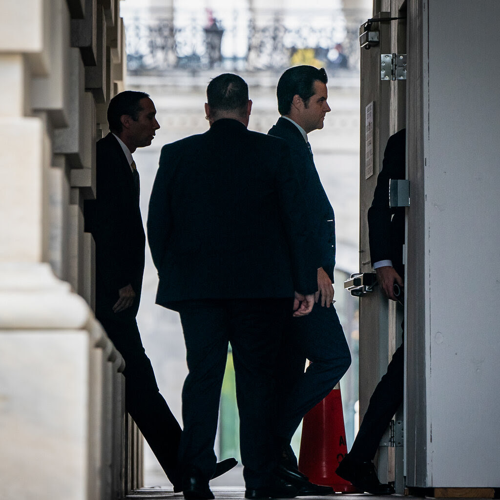 Three men walk into a door. On one side of them are a series of pillars.