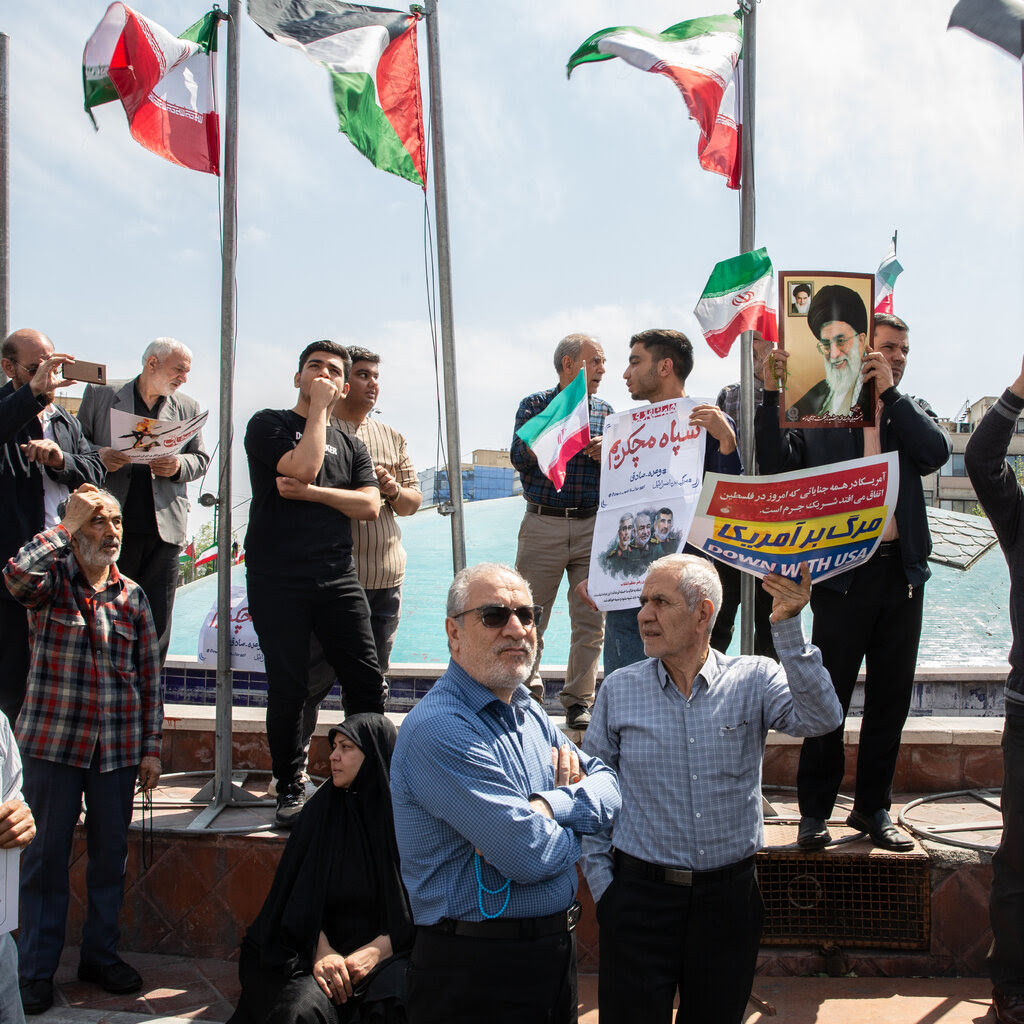 A group of people holding signs of protest against Israel and pictures of Ayatollah Ali Khamenei, Iran’s supreme leader, with Iranian flags flying behind them. 