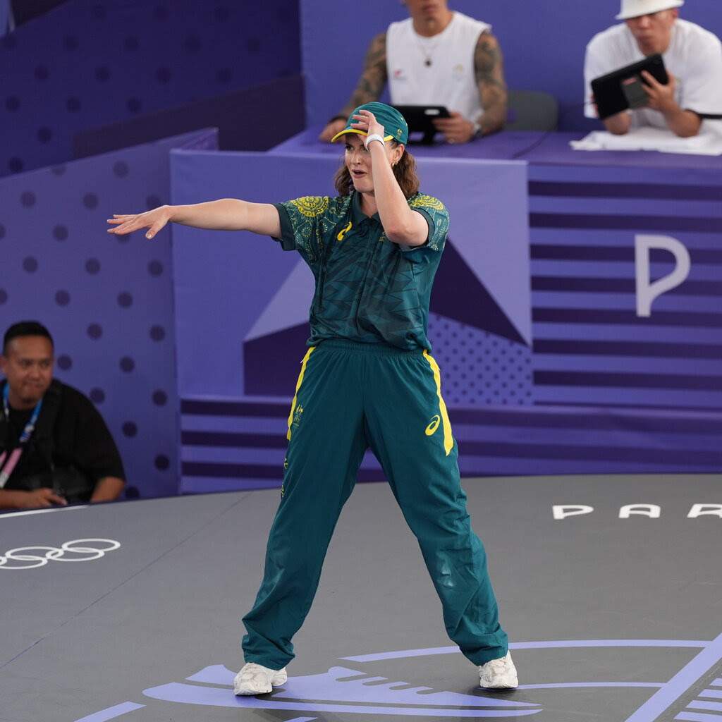 A woman in a green jersey, hat and sweatpants.