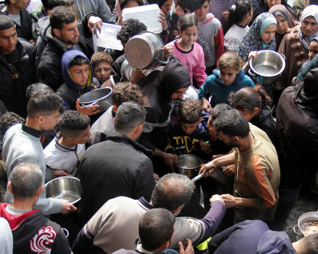 Palestinians carrying pots crowd around a food distribution site.