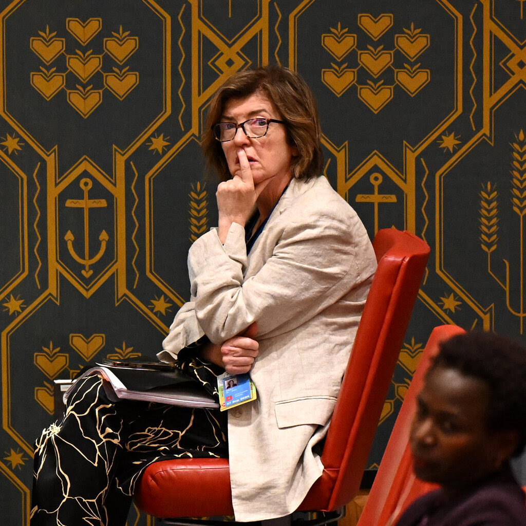 Sue Gray, the chief of staff to Britain’s prime minister, sites in a red chair and looks at the camera. She's raising her hand to her face and has a finger over her mouth.