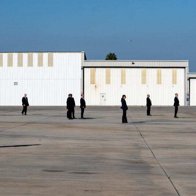 Several men and women wearing dark suits standing around an airport tarmac.