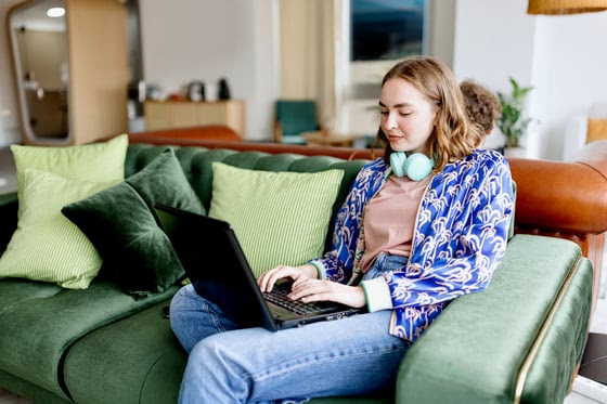Student sitting on the couch, wearing headphones, and typing on a laptop