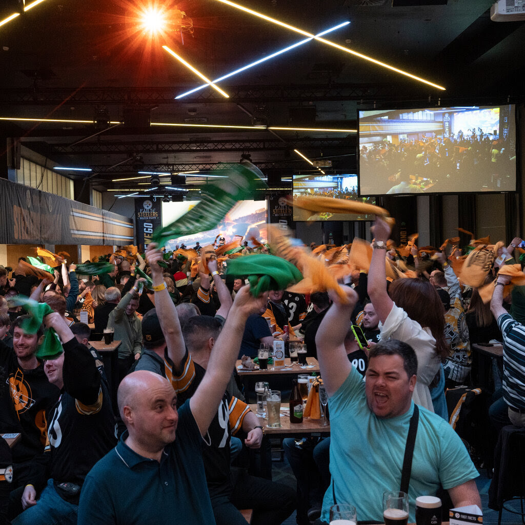 Fans cheering and twirling green and yellow towels at a bar.