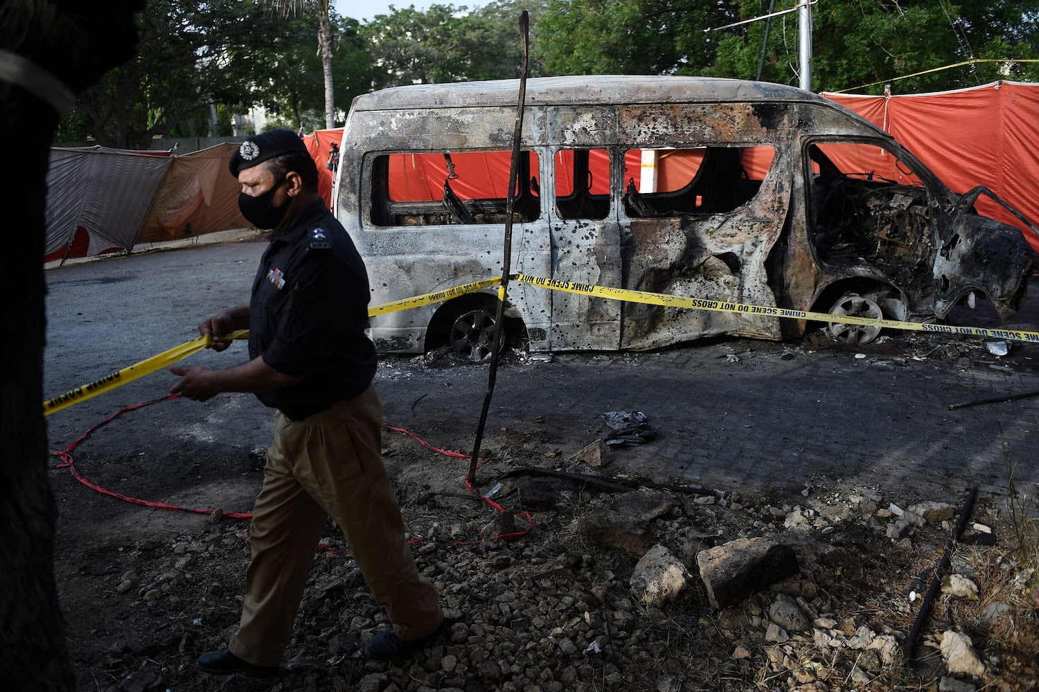 A police officer adjusts the crime scene barricade tape at the blast site a day after a suicide attack on a van near the Confucius Institute in Karachi, Pakistan.