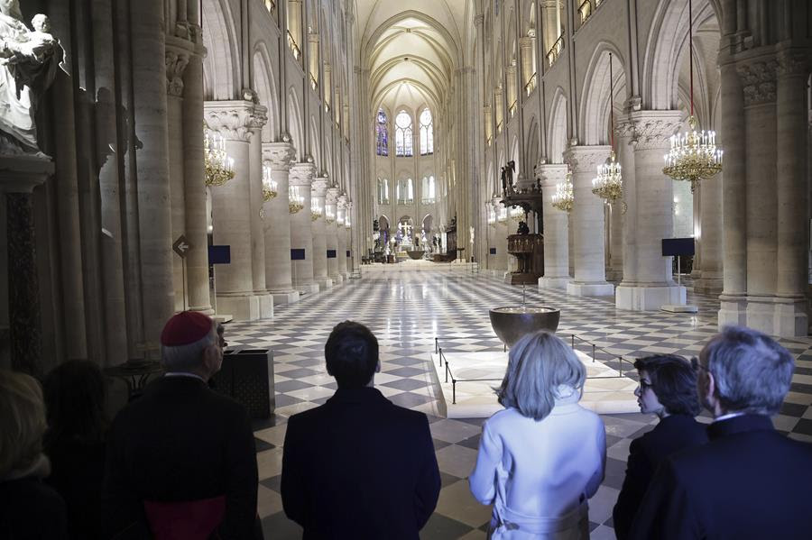 Several people stand in the entryway of the Notre Dame Cathedral. The Cathedral is well lit and recently repaired.