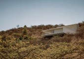 La casa parece asentarse suavemente sobre la montaña, y la parte final de la losa flota ligeramente sobre ella, apoyada en pilotes cubiertos por la misma tierra de la excavación.