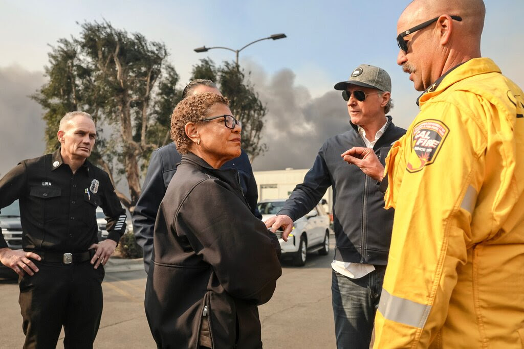 La alcaldesa Karen Bass hablaba con un grupo de funcionarios mientras se veía a lo lejos el humo de los incendios forestales.