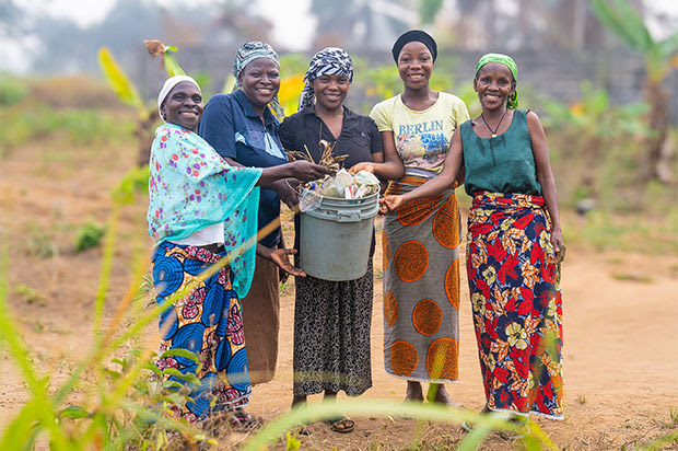 Five women standing together, holding a bucket