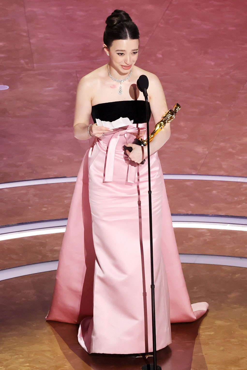 Mikey Madison making her Oscar speech on stage, in a pink and black gown.