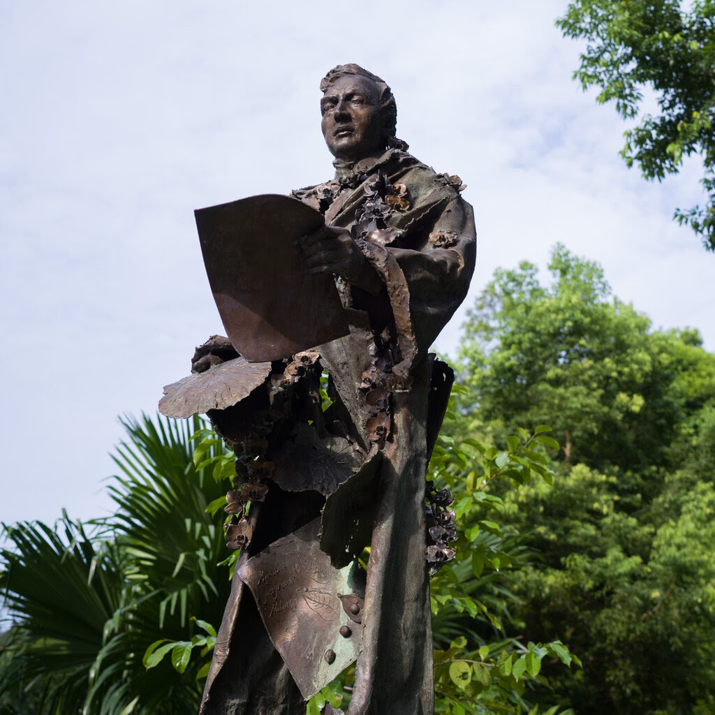 A bronze statue of a man with trees in the background. The lower torso appears to be hollowed out.