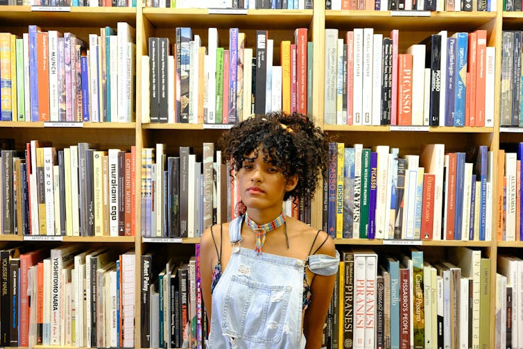 A youth in front of a bookshelf wearing overalls