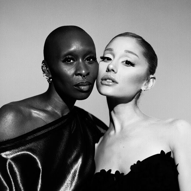 Cynthia Erivo and Ariana Grande pose cheek-to-cheek with neutral facial expressions.