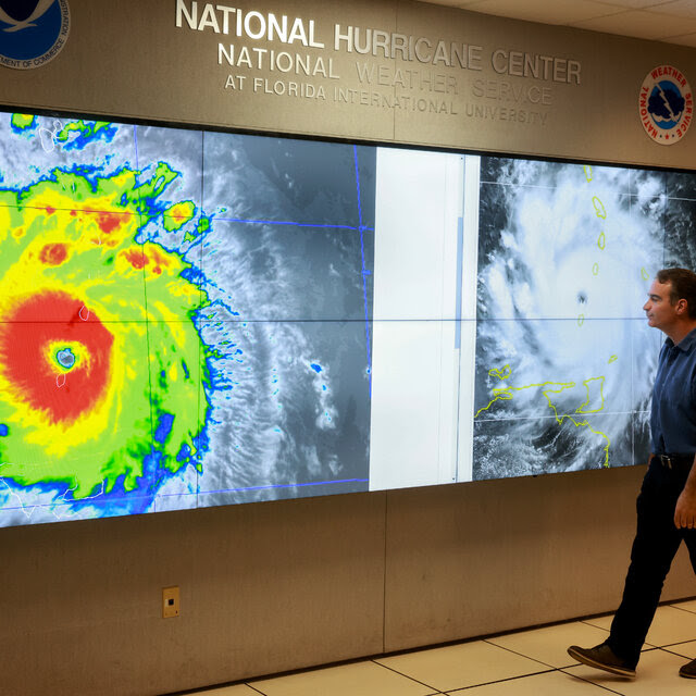 A man examines a colorful satellite image of Hurricane Beryl.