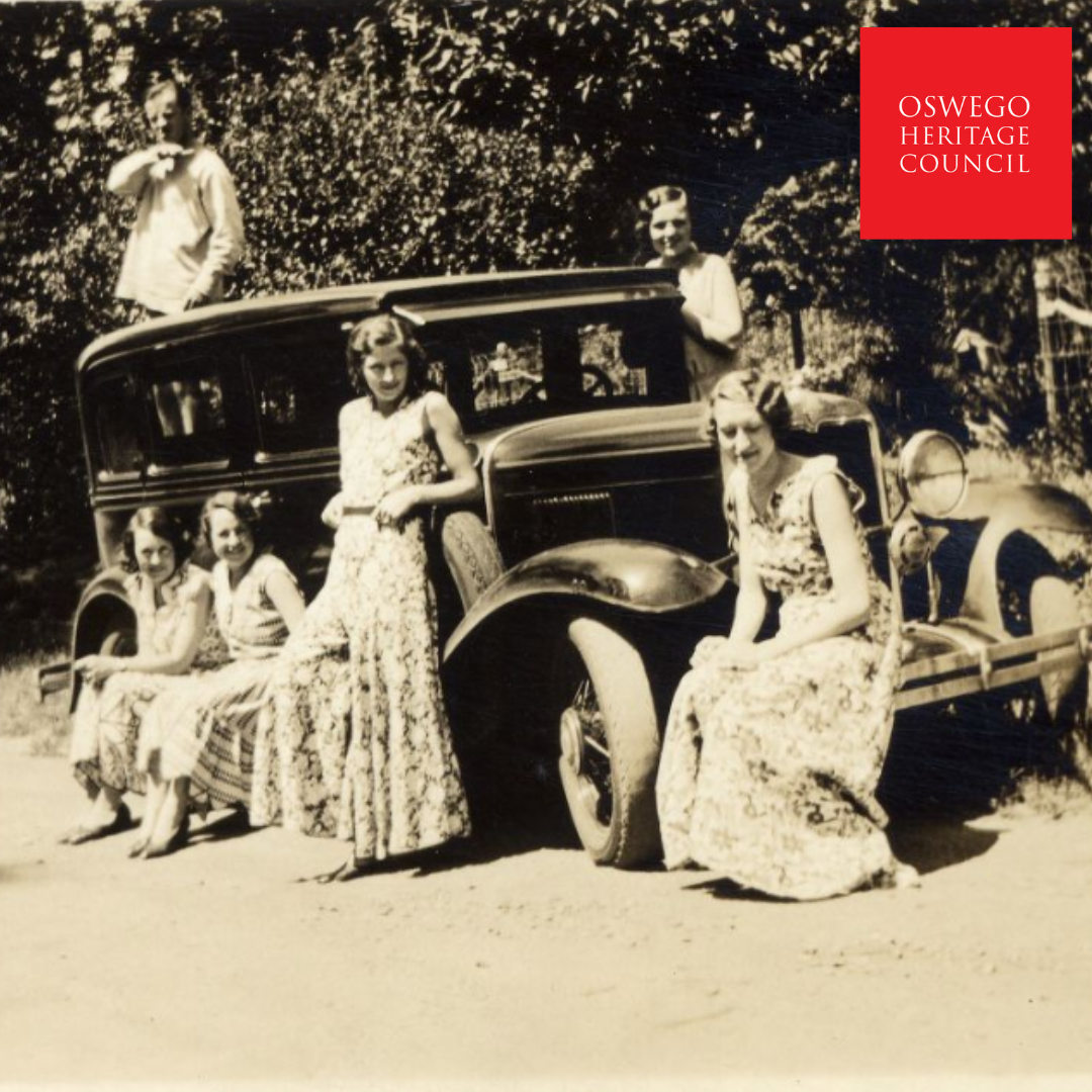 1930s photograph of a vehicle with several young girls and women sitting on it. there is one man in the background