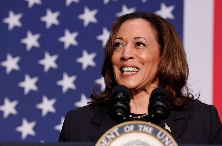 Vice President Kamala Harris stands at a podium and in front of an American flag backdrop.