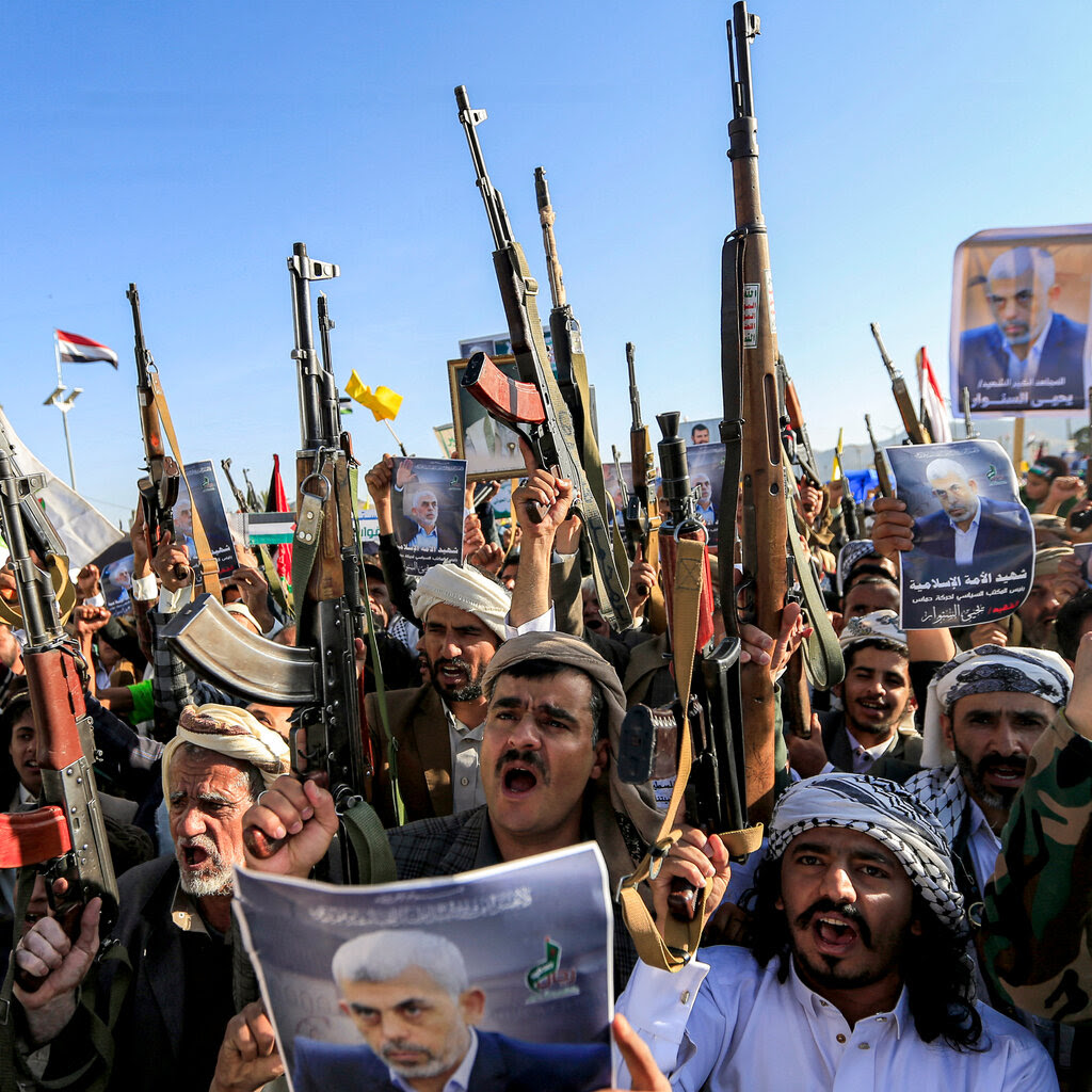 A group of protesters, with many holding rifles in the air and others holding posters with a picture of Yahya Sinwar.