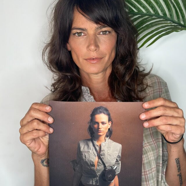 A woman with long dark hair holds up a picture of her younger self.