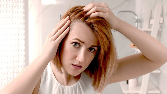 A portrait shows a woman examining her hairline. She looks concerned.