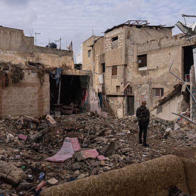 A man stands among rubble, evaluating a damaged building.